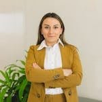 Confident woman in business suit standing indoors with crossed arms, smiling.